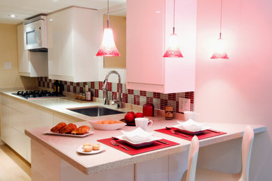 Example of a mid-sized trendy l-shaped beige floor and laminate floor kitchen design in Toronto with white cabinets, multicolored backsplash, stainless steel appliances, a peninsula, multicolored countertops, flat-panel cabinets, a single-bowl sink, quartz countertops and glass tile backsplash