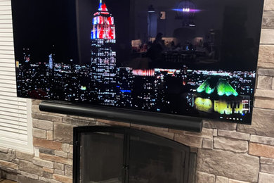 Example of a trendy dark wood floor and brown floor family room design in New York with a standard fireplace, a stone fireplace and a wall-mounted tv