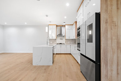 Mid-sized trendy u-shaped medium tone wood floor, brown floor and tray ceiling eat-in kitchen photo in New York with a farmhouse sink, flat-panel cabinets, white cabinets, marble countertops, gray backsplash, mosaic tile backsplash, stainless steel appliances, an island and white countertops