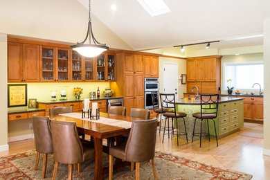 This is an example of a large traditional l-shaped eat-in kitchen in Sacramento with an undermount sink, raised-panel cabinets, light wood cabinets, granite benchtops, stainless steel appliances, light hardwood floors, with island, beige floor, green splashback and porcelain splashback.