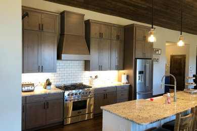 Example of an arts and crafts galley dark wood floor, brown floor and wood ceiling kitchen design in Albuquerque with a farmhouse sink, shaker cabinets, medium tone wood cabinets, granite countertops, white backsplash, subway tile backsplash, stainless steel appliances, an island and gray countertops