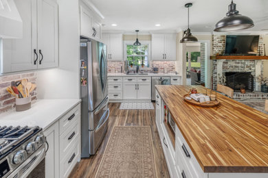 Inspiration for a mid-sized cottage vinyl floor and brown floor kitchen remodel in Atlanta with an undermount sink, shaker cabinets, white cabinets, quartz countertops, brown backsplash, brick backsplash, stainless steel appliances, an island and white countertops