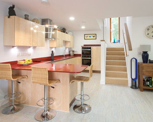 Contemporary u-shaped open plan kitchen in Other with flat-panel cabinets, a breakfast bar, a submerged sink, light wood cabinets and light hardwood flooring.