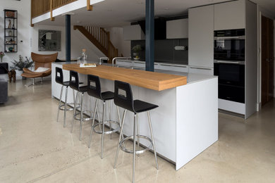 This is an example of a large contemporary single-wall open plan kitchen in Wiltshire with an integrated sink, flat-panel cabinets, grey cabinets, engineered stone countertops, black appliances and an island.