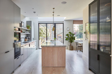Photo of a contemporary galley eat-in kitchen in London with a drop-in sink, flat-panel cabinets, black cabinets, marble benchtops, grey splashback, marble splashback, light hardwood floors, with island, brown floor and grey benchtop.