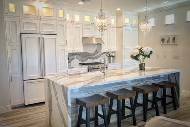 Open concept kitchen - small eclectic galley porcelain tile and white floor open concept kitchen idea in Las Vegas with an undermount sink, recessed-panel cabinets, white cabinets, quartz countertops, white backsplash, stone slab backsplash, stainless steel appliances, an island and white countertops