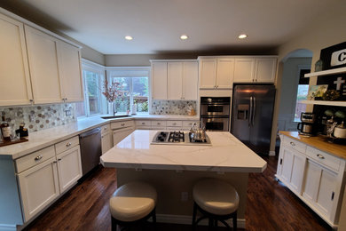 Inspiration for a transitional l-shaped open plan kitchen in Seattle with an undermount sink, shaker cabinets, white cabinets, quartz benchtops, beige splashback, glass tile splashback, stainless steel appliances, dark hardwood floors, with island, brown floor and beige benchtop.