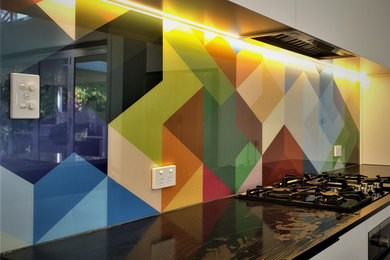 This is an example of a mid-sized contemporary single-wall eat-in kitchen in Sydney with white cabinets, solid surface benchtops, multi-coloured splashback and black benchtop.