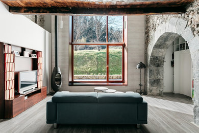 Design ideas for a country open concept living room in Bilbao with a library, white walls, painted wood floors, a wood stove, a freestanding tv and grey floor.