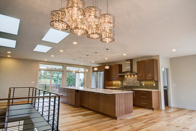 This is an example of a large contemporary galley eat-in kitchen in Seattle with an undermount sink, flat-panel cabinets, brown cabinets, solid surface benchtops, green splashback, glass tile splashback, stainless steel appliances, light hardwood floors, with island and beige floor.