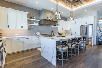 Kitchen - farmhouse medium tone wood floor kitchen idea in Phoenix with a farmhouse sink, shaker cabinets, white cabinets, quartz countertops, gray backsplash, stainless steel appliances, an island and white countertops
