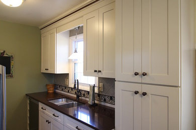 Mid-sized elegant galley medium tone wood floor and brown floor enclosed kitchen photo in Other with a double-bowl sink, shaker cabinets, white cabinets, quartz countertops, gray backsplash, porcelain backsplash, stainless steel appliances and no island