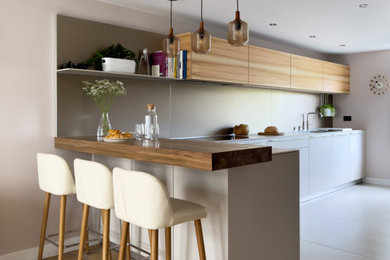 This is an example of a small contemporary galley open plan kitchen in Other with an integrated sink, flat-panel cabinets, grey cabinets, laminate countertops, metallic splashback, metal splashback, black appliances, porcelain flooring, a breakfast bar and grey worktops.