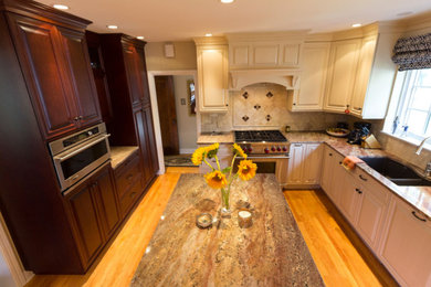 Eat-in kitchen - large traditional u-shaped medium tone wood floor and brown floor eat-in kitchen idea in Denver with raised-panel cabinets, granite countertops, beige backsplash, stone tile backsplash, stainless steel appliances, an island, an undermount sink and beige cabinets