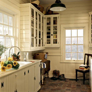 Photo of a country utility room in New York with a built-in sink, glass-front cabinets, white cabinets, tile countertops, white walls and a side by side washer and dryer.
