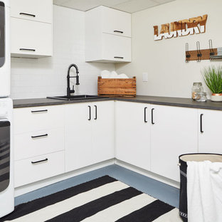 トロントのカントリー風おしゃれな洗濯室 (ドロップインシンク、フラットパネル扉のキャビネット、白いキャビネット、グレーの壁、上下配置の洗濯機・乾燥機、青い床、グレーのキッチンカウンター) の写真