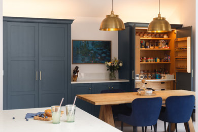 Photo of a medium sized classic l-shaped kitchen/diner in Other with shaker cabinets, blue cabinets, quartz worktops, white splashback, engineered quartz splashback, an island, white worktops, black appliances, porcelain flooring, grey floors, a vaulted ceiling and a chimney breast.