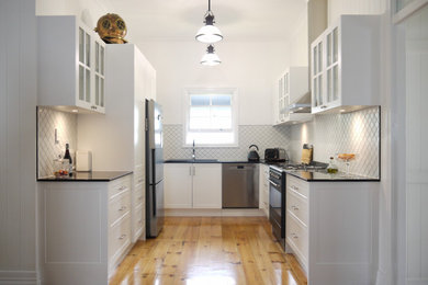 Inspiration for a small u-shaped separate kitchen in Sunshine Coast with a double-bowl sink, recessed-panel cabinets, white cabinets, quartz benchtops, black appliances, medium hardwood floors and black benchtop.