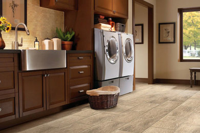 Dedicated laundry room - mid-sized rustic single-wall slate floor dedicated laundry room idea in Denver with a farmhouse sink, raised-panel cabinets, medium tone wood cabinets, beige walls and a side-by-side washer/dryer