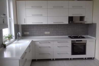На фото: кухня в современном стиле с плоскими фасадами, белыми фасадами, серым фартуком, фартуком из керамической плитки и техникой из нержавеющей стали с