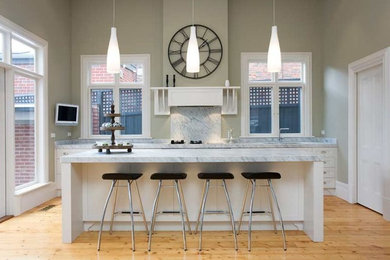 Mid-sized modern single-wall open plan kitchen in Melbourne with a double-bowl sink, shaker cabinets, white cabinets, marble benchtops, white splashback, stone slab splashback, stainless steel appliances, light hardwood floors and with island.