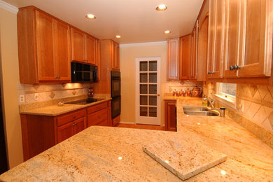 Enclosed kitchen - mid-sized traditional u-shaped light wood floor and brown floor enclosed kitchen idea in DC Metro with a double-bowl sink, recessed-panel cabinets, light wood cabinets, granite countertops, beige backsplash, stone tile backsplash, black appliances and a peninsula