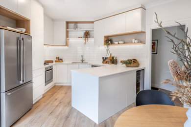 Small contemporary u-shaped eat-in kitchen in Adelaide with an undermount sink, flat-panel cabinets, white cabinets, quartz benchtops, white splashback, subway tile splashback, stainless steel appliances, laminate floors, a peninsula, brown floor and white benchtop.