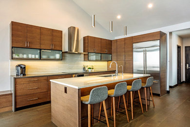 Example of a mid-sized trendy l-shaped medium tone wood floor and brown floor eat-in kitchen design in Denver with a double-bowl sink, flat-panel cabinets, brown cabinets, solid surface countertops, beige backsplash, stone slab backsplash, stainless steel appliances, an island and beige countertops