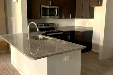 Example of a large minimalist l-shaped laminate floor and gray floor eat-in kitchen design in Atlanta with a drop-in sink, flat-panel cabinets, dark wood cabinets, granite countertops, gray backsplash, granite backsplash, stainless steel appliances, an island and gray countertops