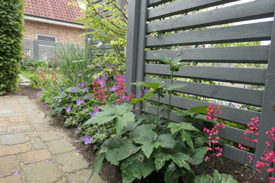Mittelgroßer Country Garten im Sommer, neben dem Haus mit Blumenbeet, direkter Sonneneinstrahlung und Holzzaun in Hamburg