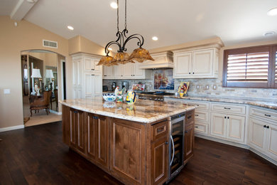 Inspiration for a large timeless u-shaped dark wood floor eat-in kitchen remodel in Orange County with a farmhouse sink, raised-panel cabinets, white cabinets, granite countertops, beige backsplash, stone tile backsplash, stainless steel appliances and an island