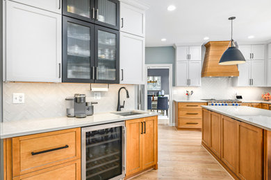 Transitional eat-in kitchen in DC Metro with a farmhouse sink, recessed-panel cabinets, white cabinets, quartzite benchtops, white splashback, ceramic splashback, stainless steel appliances, light hardwood floors, with island, brown floor and beige benchtop.