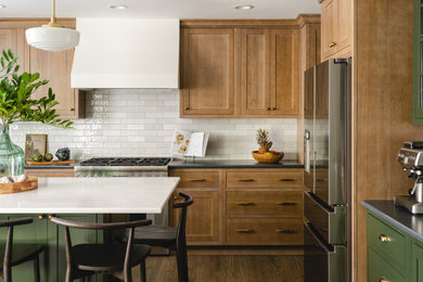 Example of a transitional l-shaped medium tone wood floor kitchen design in Kansas City with shaker cabinets, light wood cabinets, quartz countertops, white backsplash, ceramic backsplash, stainless steel appliances and an island