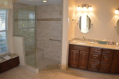 Corner shower - mid-sized traditional master beige tile and ceramic tile travertine floor corner shower idea in Orange County with raised-panel cabinets, dark wood cabinets, a one-piece toilet, beige walls, an undermount sink and granite countertops