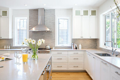 This is an example of a large transitional l-shaped eat-in kitchen in Vancouver with an undermount sink, shaker cabinets, white cabinets, quartz benchtops, grey splashback, matchstick tile splashback, stainless steel appliances, medium hardwood floors, with island, brown floor and grey benchtop.