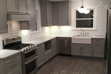 Example of a transitional ceramic tile kitchen design in Other with a farmhouse sink, raised-panel cabinets, gray cabinets, white backsplash, subway tile backsplash, stainless steel appliances and an island