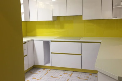 Medium sized contemporary u-shaped enclosed kitchen in Hertfordshire with a double-bowl sink, flat-panel cabinets, yellow cabinets, laminate countertops, yellow splashback, glass sheet splashback, white appliances, vinyl flooring, no island, yellow floors and white worktops.