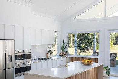 Expansive beach style eat-in kitchen in Central Coast with a farmhouse sink, white cabinets, quartz benchtops, stainless steel appliances, ceramic floors, with island, white benchtop, vaulted, white splashback and engineered quartz splashback.