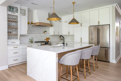 Inspiration for a mid-sized transitional laminate floor and brown floor open concept kitchen remodel in Raleigh with an undermount sink, shaker cabinets, white cabinets, quartz countertops, white backsplash, quartz backsplash, stainless steel appliances, an island and white countertops