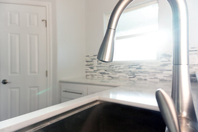 Example of a beach style u-shaped kitchen design in Houston with an undermount sink, shaker cabinets, white cabinets, quartzite countertops, multicolored backsplash, glass tile backsplash, stainless steel appliances and white countertops