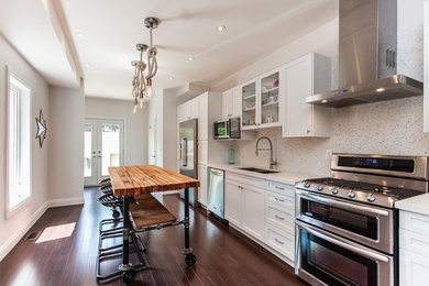 Mid-sized transitional single-wall eat-in kitchen in Toronto with a double-bowl sink, shaker cabinets, white cabinets, quartz benchtops, white splashback, mosaic tile splashback, stainless steel appliances, dark hardwood floors and with island.