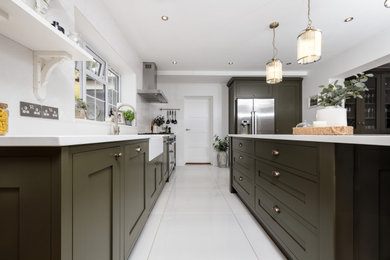 Design ideas for a classic kitchen/diner in Berkshire with a belfast sink, shaker cabinets, green cabinets, engineered stone countertops, white splashback, ceramic splashback, stainless steel appliances, ceramic flooring, an island, white floors and white worktops.