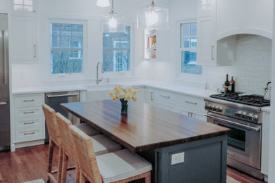 Example of a transitional l-shaped medium tone wood floor eat-in kitchen design in Philadelphia with a farmhouse sink, white cabinets, white backsplash, subway tile backsplash, stainless steel appliances, an island and white countertops