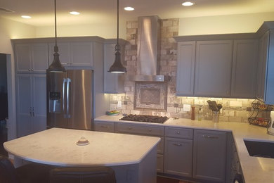 Mid-sized transitional l-shaped eat-in kitchen in Milwaukee with an undermount sink, recessed-panel cabinets, grey cabinets, quartz benchtops, grey splashback, stone tile splashback, stainless steel appliances, laminate floors and with island.
