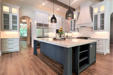 Inspiration for a large transitional medium tone wood floor kitchen remodel in Houston with an undermount sink, shaker cabinets, white cabinets, quartzite countertops, white backsplash, ceramic backsplash, stainless steel appliances, an island and white countertops