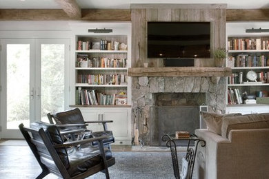 Photo of a country living room in New York with white walls, dark hardwood floors, a standard fireplace, a stone fireplace surround and a wall-mounted tv.