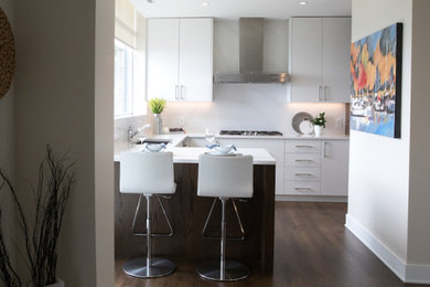Inspiration for a mid-sized contemporary l-shaped dark wood floor and brown floor kitchen pantry remodel in Vancouver with a drop-in sink, flat-panel cabinets, white cabinets, quartz countertops, white backsplash, quartz backsplash, stainless steel appliances, a peninsula and white countertops