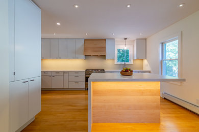 Inspiration for a mid-sized modern u-shaped medium tone wood floor and yellow floor eat-in kitchen remodel in Burlington with an undermount sink, flat-panel cabinets, white cabinets, quartzite countertops, beige backsplash, glass tile backsplash, stainless steel appliances, an island and white countertops