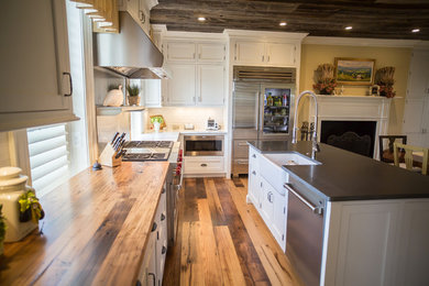 Inspiration for a large farmhouse l-shaped light wood floor and brown floor open concept kitchen remodel in DC Metro with a farmhouse sink, shaker cabinets, white cabinets, wood countertops, white backsplash, subway tile backsplash, stainless steel appliances and an island