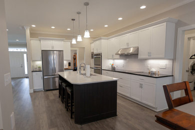 Example of a minimalist vinyl floor kitchen design in Other with a double-bowl sink, shaker cabinets, white cabinets, quartz countertops, white backsplash, ceramic backsplash, stainless steel appliances, an island and black countertops